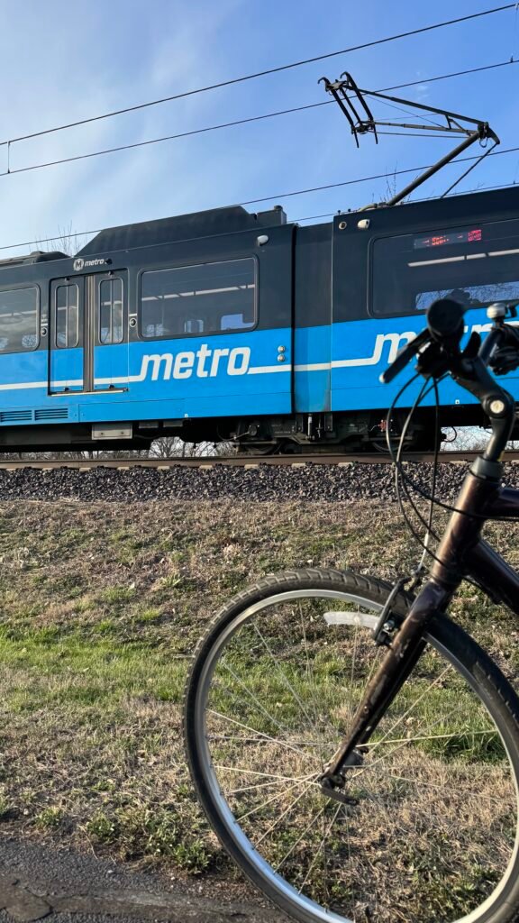 A bicycle sits along the MetroBikeLink Trail with a train passing by in the background.