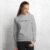 A woman models the Bike Rides > Brain Rot hoodie in athletic heather against a painted white brick wall.