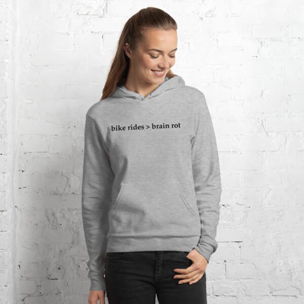 A woman models the Bike Rides > Brain Rot hoodie in athletic heather against a painted white brick wall.
