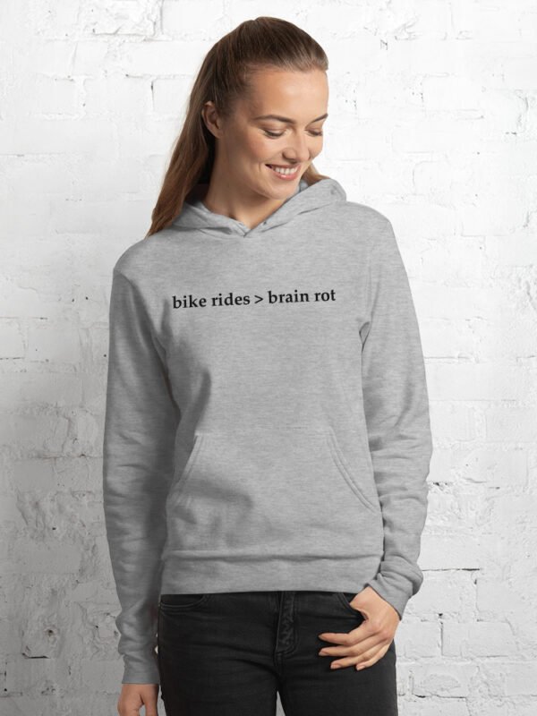 A woman models the Bike Rides > Brain Rot hoodie in athletic heather against a painted white brick wall.