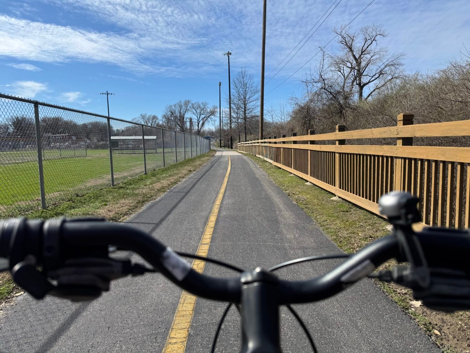 A POV shot of a bicycle riding between a creek bed and baseball field along the Richland Creek Greenway.